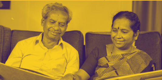 A smiling man and woman of South Asian heritage, look at a photo album together. Image taken from Memory Club poster.